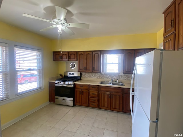 kitchen with freestanding refrigerator, a ceiling fan, light countertops, a sink, and gas stove