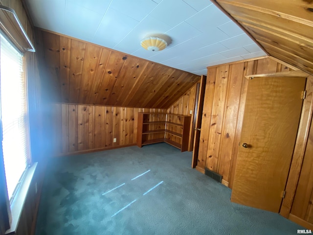 additional living space featuring visible vents, wood walls, vaulted ceiling, and carpet
