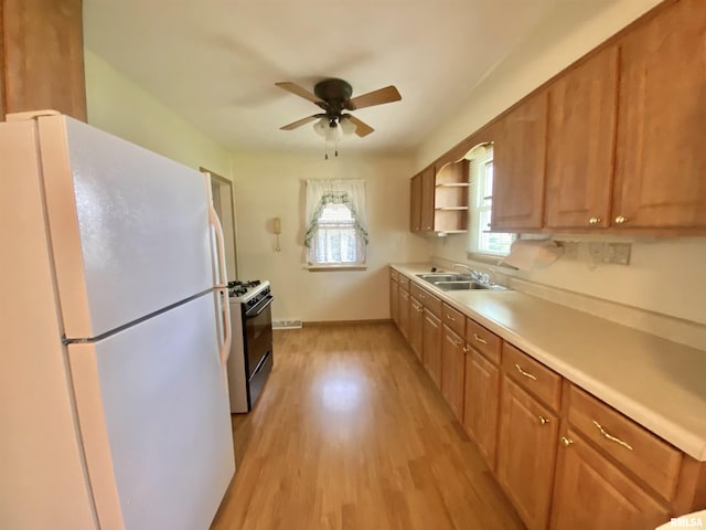 kitchen featuring a sink, freestanding refrigerator, gas range oven, ceiling fan, and light countertops