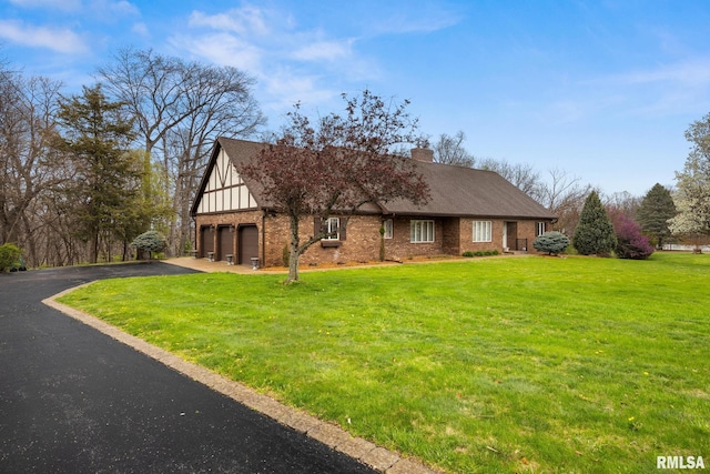 view of front of property with a chimney, driveway, brick siding, a garage, and a front lawn