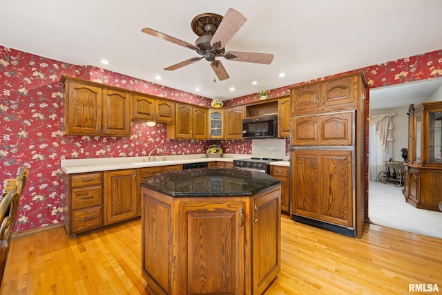 kitchen featuring a center island, wallpapered walls, light wood-type flooring, ceiling fan, and appliances with stainless steel finishes