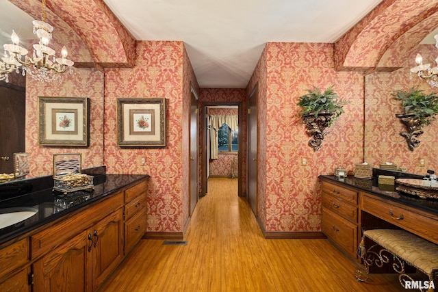 hall featuring a chandelier, baseboards, wallpapered walls, and light wood-style floors