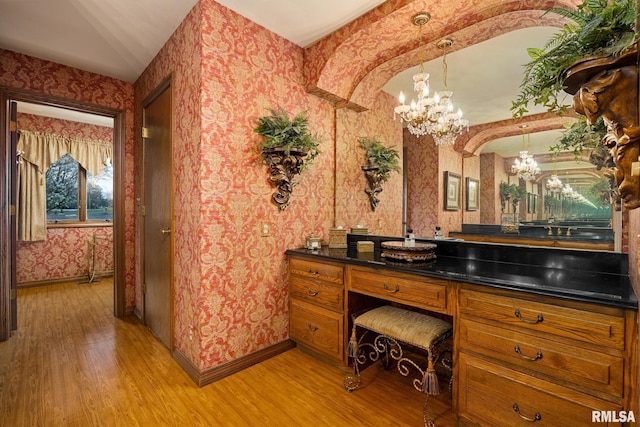 bathroom featuring a notable chandelier, baseboards, wallpapered walls, and wood finished floors