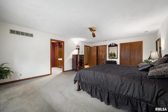 bedroom with baseboards, ensuite bathroom, visible vents, two closets, and light carpet