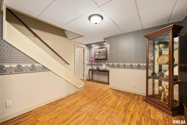 finished below grade area with wood finished floors, wallpapered walls, a paneled ceiling, baseboards, and stairs