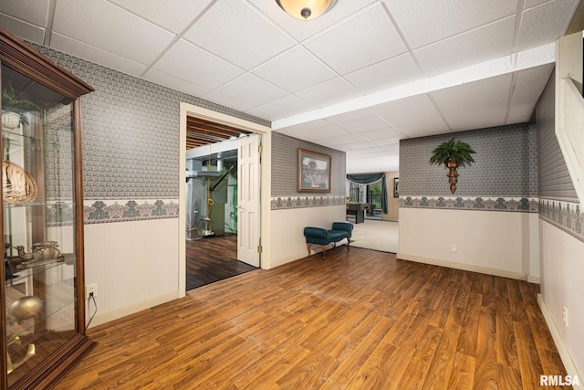 spare room featuring wood finished floors, baseboards, wallpapered walls, and a drop ceiling