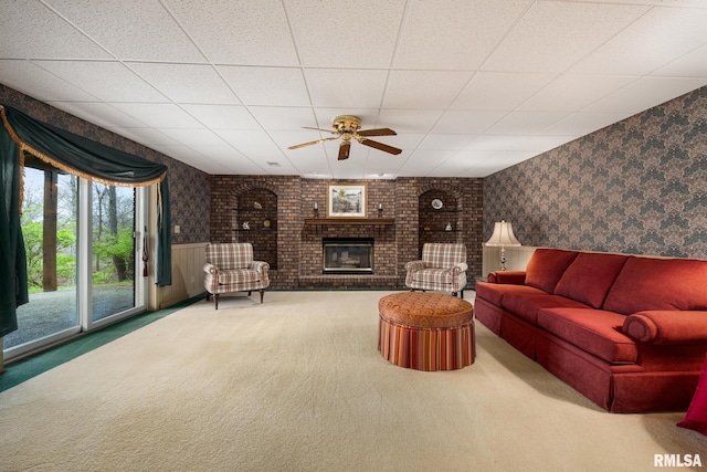 carpeted living room featuring wallpapered walls, a fireplace, a paneled ceiling, wainscoting, and ceiling fan