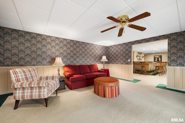 carpeted living room featuring a wainscoted wall, a drop ceiling, and wallpapered walls