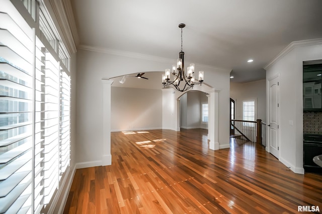 unfurnished dining area featuring arched walkways, ornamental molding, an inviting chandelier, and wood finished floors