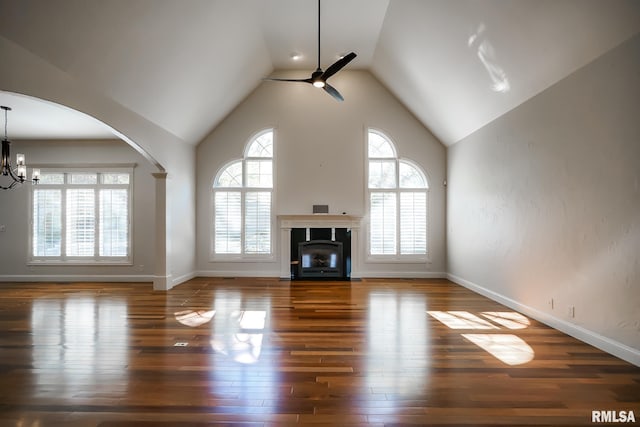 unfurnished living room featuring wood finished floors, ceiling fan with notable chandelier, high vaulted ceiling, baseboards, and arched walkways