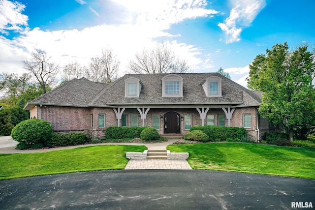 view of front of property with a shingled roof, brick siding, and a front lawn