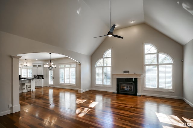 unfurnished living room with a wealth of natural light, dark wood-style flooring, ceiling fan with notable chandelier, and a fireplace with flush hearth