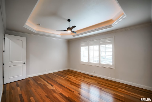 spare room featuring baseboards, wood-type flooring, ceiling fan, crown molding, and a raised ceiling