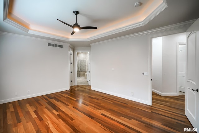 unfurnished bedroom with wood finished floors, a tray ceiling, visible vents, baseboards, and ornamental molding