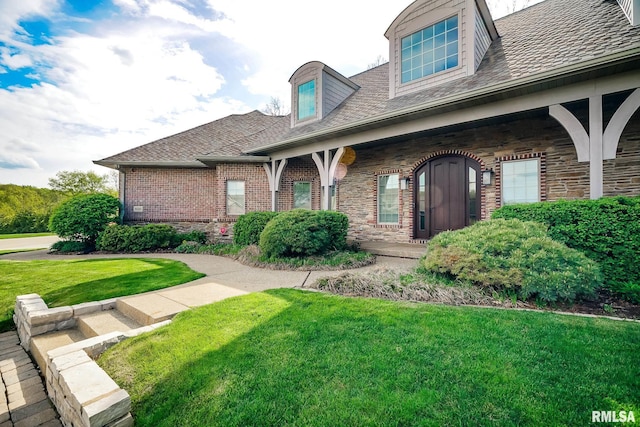 view of front of property with a shingled roof, brick siding, a front yard, and stone siding