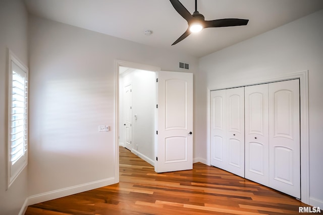 unfurnished bedroom with a closet, wood finished floors, visible vents, ceiling fan, and baseboards
