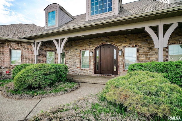 view of exterior entry featuring a porch, a shingled roof, and stone siding