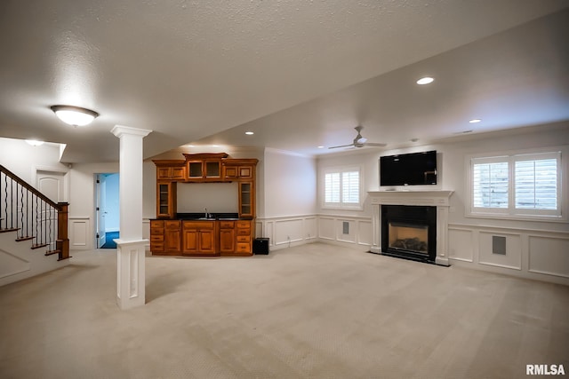unfurnished living room with light carpet, a decorative wall, ceiling fan, and a sink