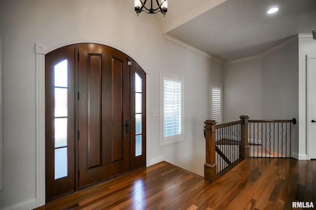 foyer featuring a notable chandelier, baseboards, crown molding, dark wood-type flooring, and arched walkways