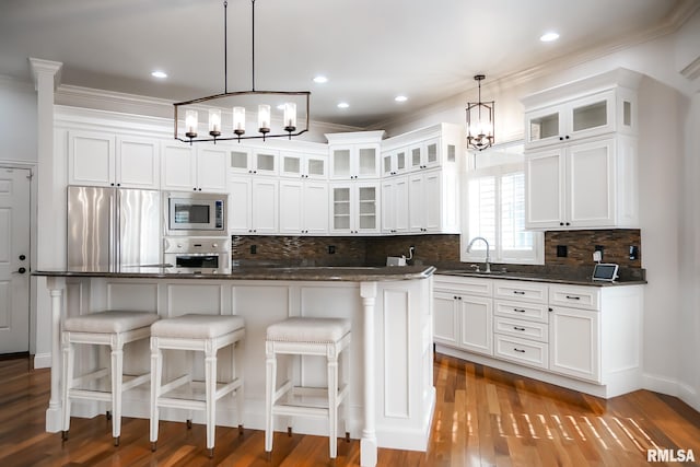 kitchen featuring a sink, stainless steel appliances, crown molding, white cabinetry, and a chandelier