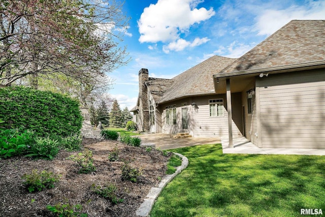 rear view of property featuring a chimney, a yard, a patio area, and a shingled roof