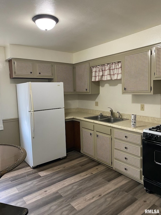 kitchen featuring a sink, freestanding refrigerator, black range with gas cooktop, light countertops, and dark wood-style floors
