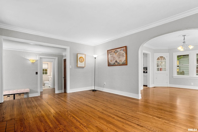 2714 W Kenwood Ave, West Peoria, IL 61604 - unfurnished living room featuring a chandelier, arched walkways, wood finished floors, crown molding, and baseboards