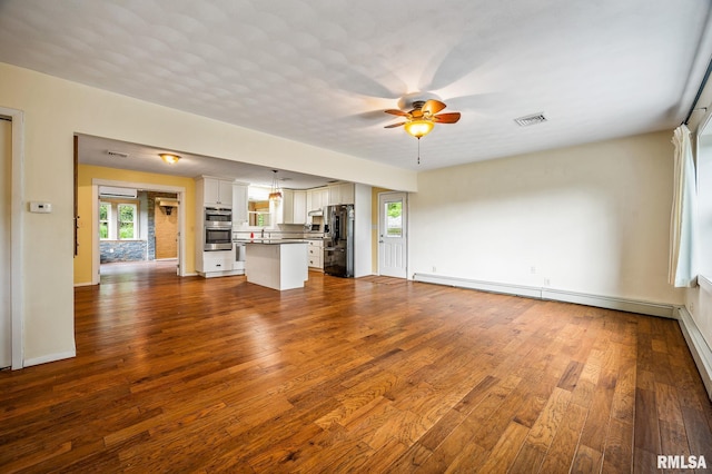 21016 N US Highway 24, Canton, IL 61520 - unfurnished living room featuring a wall mounted AC, baseboards, dark wood finished floors, ceiling fan, and visible vents