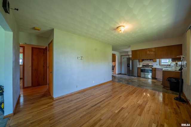 unfurnished living room with hardwood / wood-style floors, plenty of natural light, baseboards, and a sink