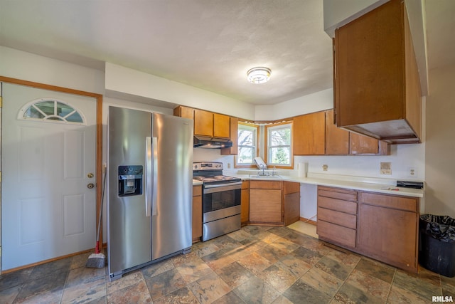 kitchen featuring appliances with stainless steel finishes, under cabinet range hood, light countertops, brown cabinets, and dark stone finish floors