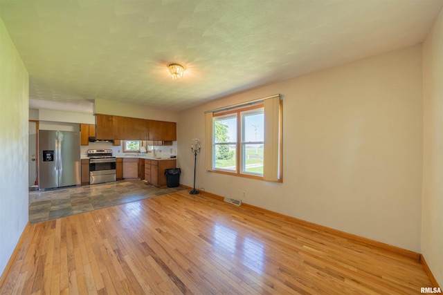 kitchen featuring stainless steel appliances, brown cabinetry, light countertops, hardwood / wood-style flooring, and baseboards