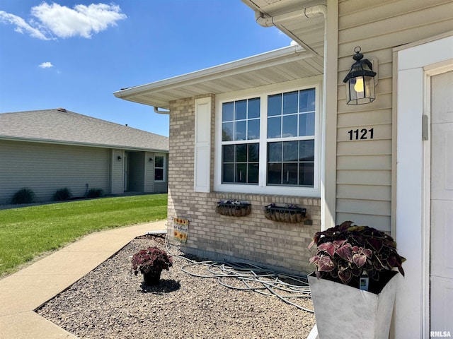 view of exterior entry featuring brick siding and a lawn