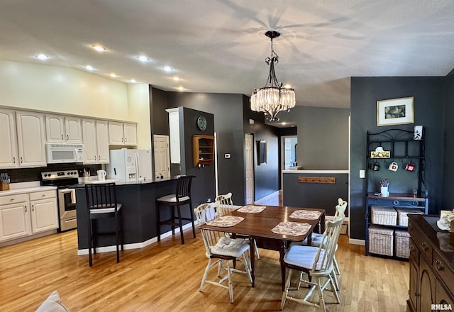 dining space with a chandelier, light wood-style floors, baseboards, recessed lighting, and a towering ceiling