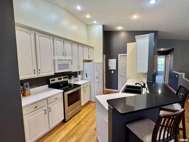 kitchen with white appliances, a sink, a breakfast bar, light wood-style floors, and a peninsula