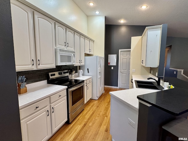 kitchen with white appliances, a sink, tasteful backsplash, light wood finished floors, and white cabinets