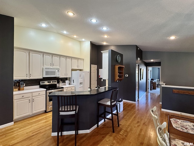kitchen featuring white appliances, a kitchen bar, a textured ceiling, light wood-style floors, and tasteful backsplash