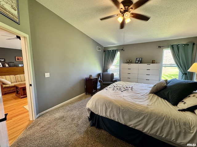 bedroom featuring multiple windows, a textured ceiling, baseboards, ceiling fan, and light colored carpet