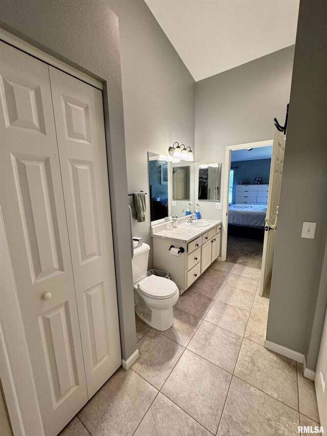 ensuite bathroom featuring vanity, toilet, tile patterned floors, high vaulted ceiling, and a closet