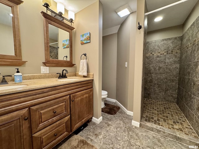 bathroom featuring a tile shower, toilet, double vanity, tile patterned flooring, and baseboards