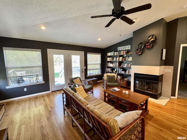 living room with a textured ceiling, wood finished floors, lofted ceiling, a tiled fireplace, and a ceiling fan
