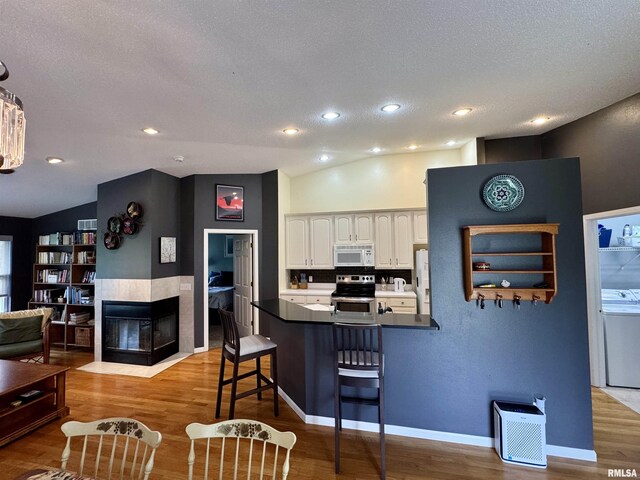 kitchen with white appliances, washer / clothes dryer, a peninsula, white cabinetry, and a kitchen bar