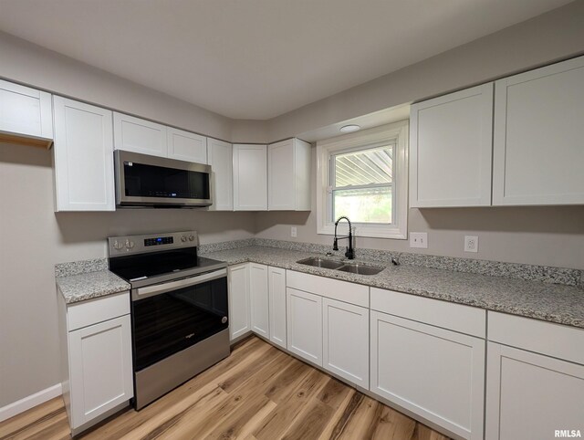 kitchen with appliances with stainless steel finishes, a sink, white cabinetry, light wood-style floors, and light stone countertops