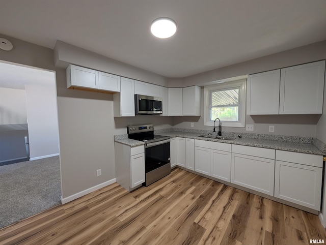 kitchen with stainless steel appliances, a sink, light stone counters, white cabinetry, and light wood-type flooring