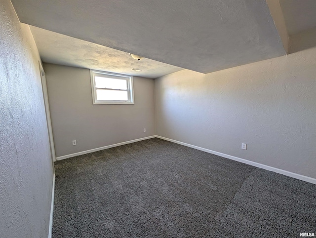 spare room featuring dark colored carpet, baseboards, and a textured wall