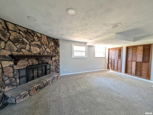 unfurnished living room featuring baseboards, a stone fireplace, carpet, and a textured ceiling