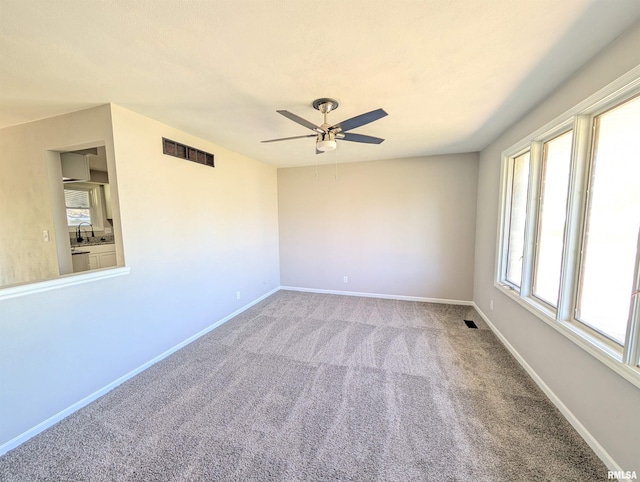 carpeted spare room with ceiling fan, a sink, and baseboards
