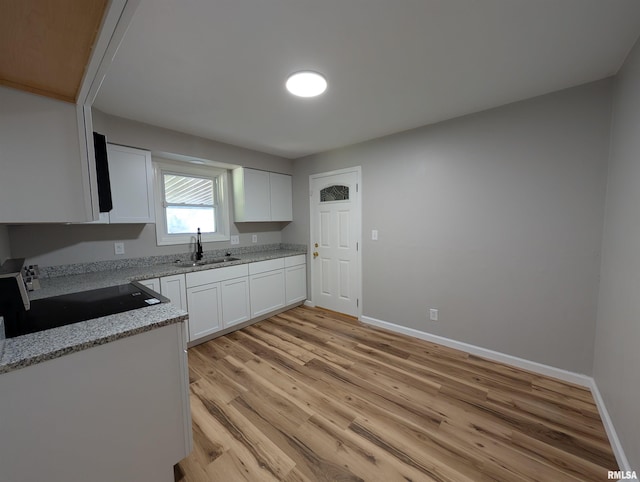 kitchen featuring stove, a sink, light wood-style floors, white cabinets, and baseboards