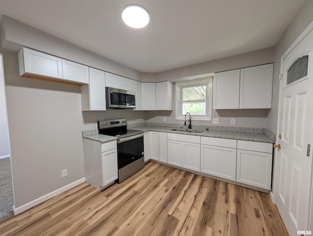 kitchen with appliances with stainless steel finishes, a sink, white cabinets, and light wood-type flooring