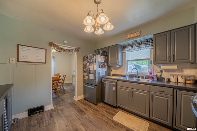kitchen with stainless steel appliances, a sink, gray cabinetry, a chandelier, and dark wood-type flooring