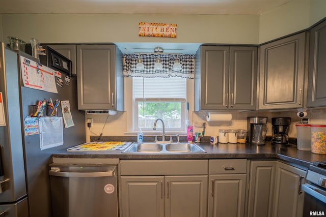 kitchen with stainless steel appliances, a sink, dark countertops, gray cabinetry, and decorative backsplash